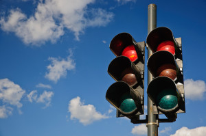 A couple of traffic lights installations with the red ones turned on and the green and yellow off captured against a blue sky with several white clouds scattered over.